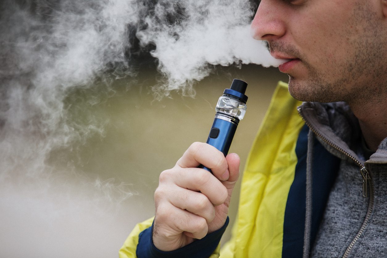 A Man in a Yellow Jacket is Vaping with a Blue Vape Pen