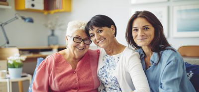 Three women of several generations sit on a couch and embrace for a photo. 