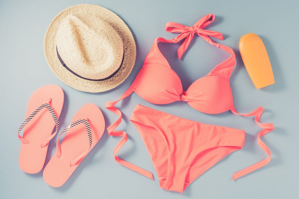 Pink swimsuit with beach accessories on blue background