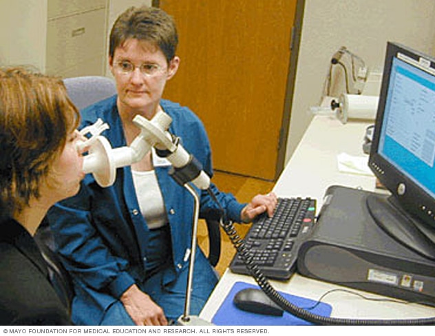 Woman using spirometer, assisted by technician